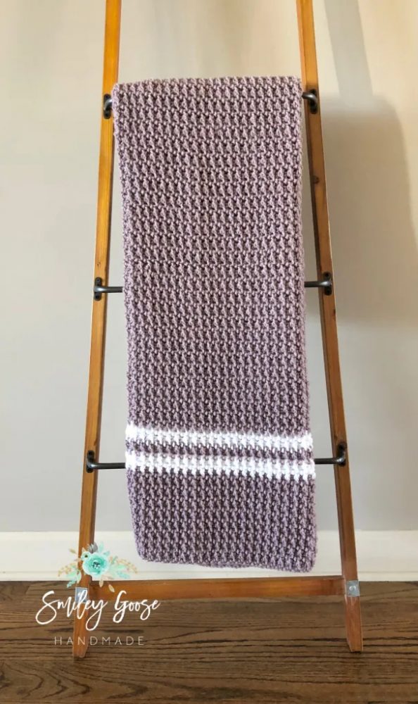 the Ava Baby Crochet Blanket on a wooden standing hanger