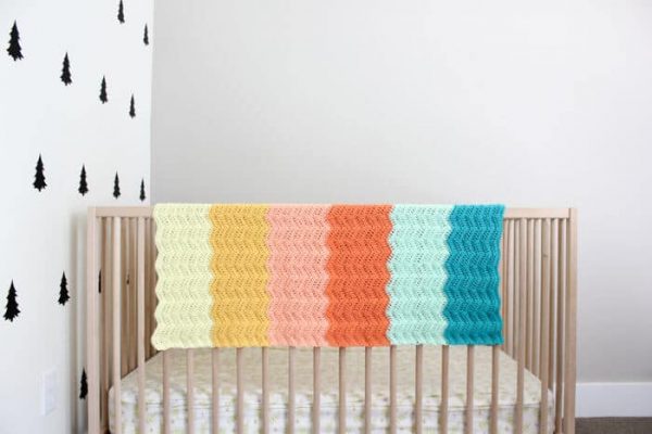 A modern crochet baby blanket on a crib
