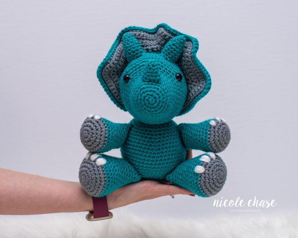 a person holding tanner the triceratops crochet dinosaur by nicole chase